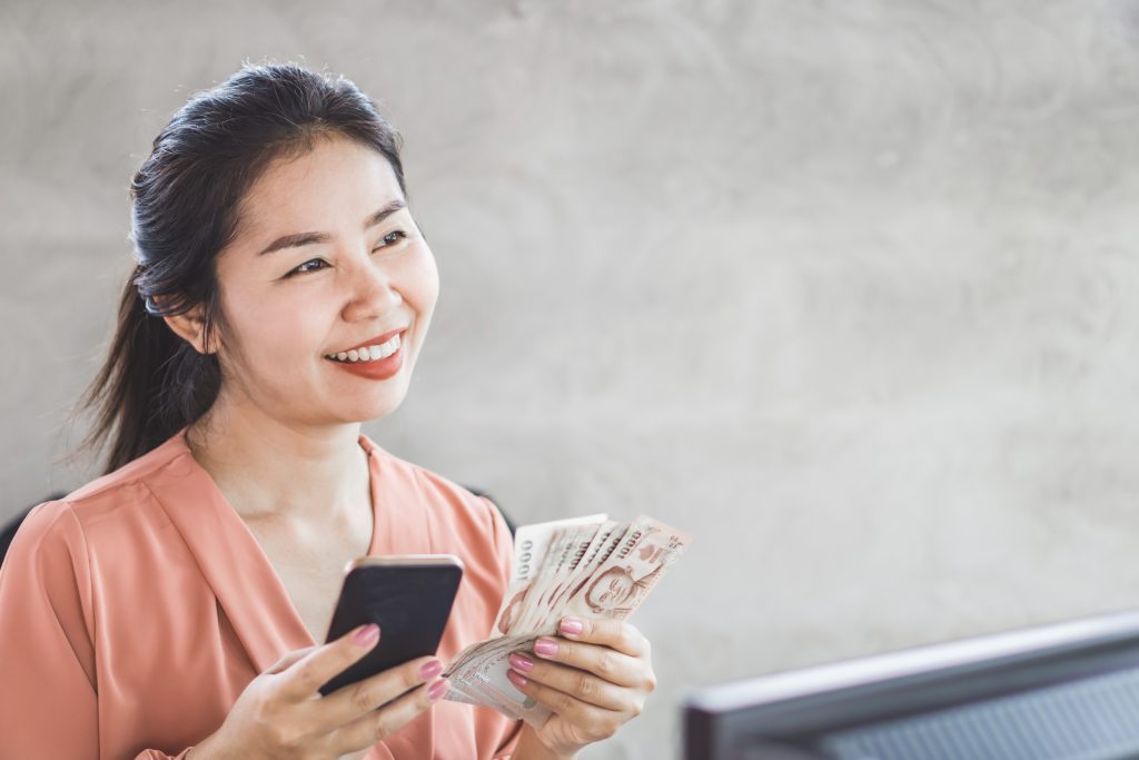 Happy Asian woman holding Smartphone and banknotes in Signal Mountain, TN